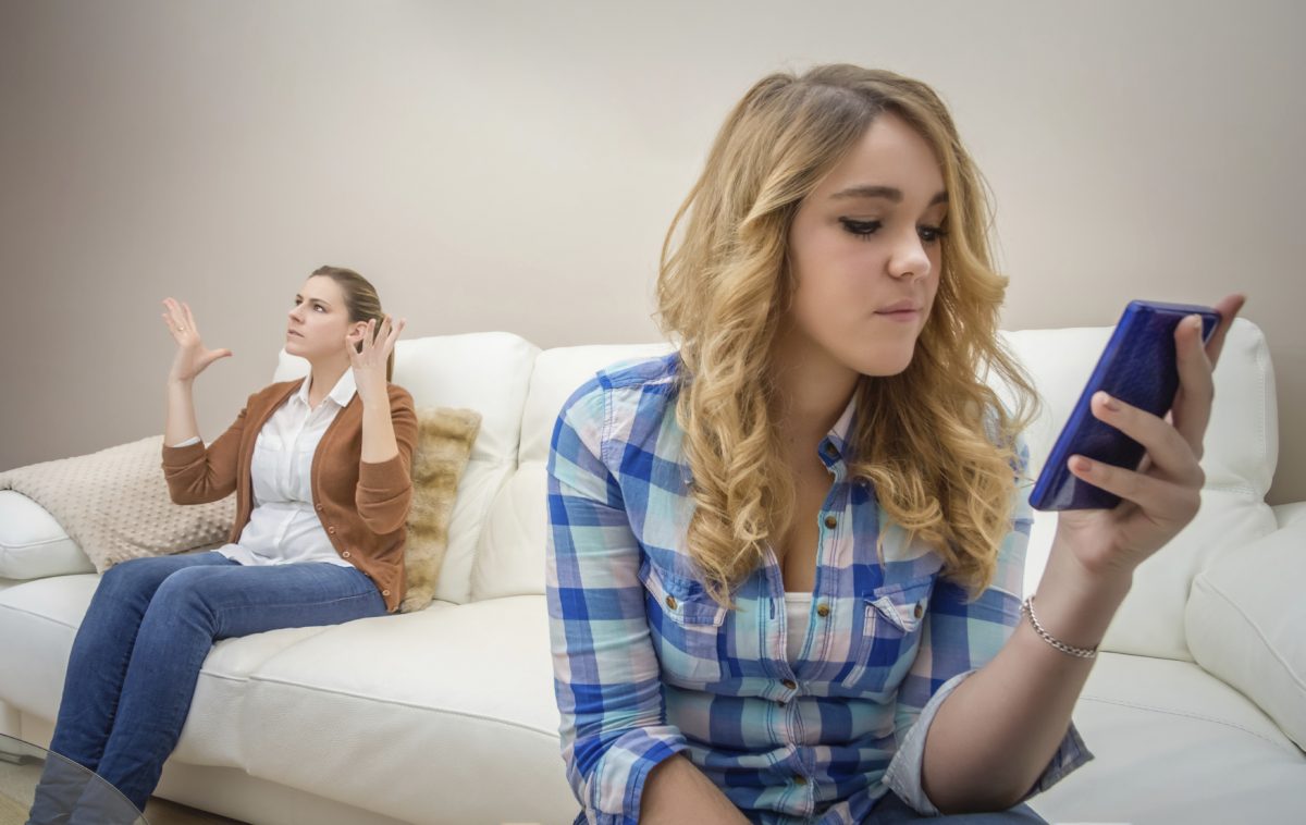 A teen looks at her phone while a parent tries to get their attention. This could represent behavior issues a teen therapist in Phoenix, AZ can address. Learn more about counseling for teens in Phoenix, AZ and counseling for teens in Arcadia, AZ today.