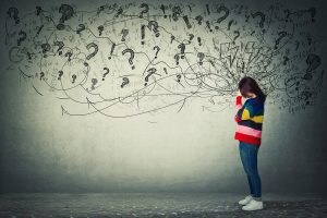 A woman hides her face while question marks and exclamation points surround her head. Trauma therapy in Arcadia, AZ can offer support in overcoming symptoms of PTSD. Learn more by contacting a therapist in Arcadia, AZ today. 