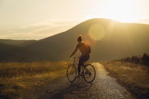 A woman rides a bike along a gravel road in the light of the setting sun. Online anxiety treatment in Arcadia, AZ can equip you with the tools to overcome anxious symptoms. Learn more about anxiety treatment in Biltmore, AZ by contacting an anxiety therapist in Arcadia, AZ today.