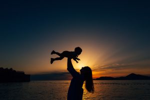 A mother holds their baby above their head against the light of the morning sun. A parenting counselor in Arcadia, AZ can offer support with attachment parenting in Phoenix, AZ and other services. Learn more about counseling for parents in Phoenix, AZ and other services.