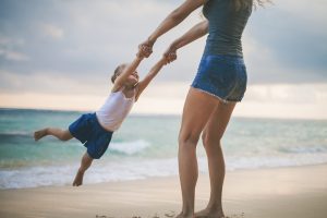 A child smiles as their parent spins them around by the arms. Learn how counseling for parents in Phoenix, AZ can offer support by searching "attachment parenting in Phoenix, AZ" or counseling for parents in Phoenix, AZ today.