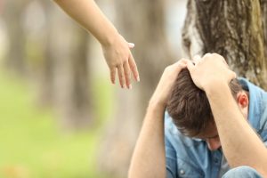 A person offers their hand in support towards an upset man sitting. This represents the support a therapist in Arcadia, AZ can offer. Learn more about trauma therapy in Arcadia, AZ and the support therapy in Arcadia, AZ can offer. 