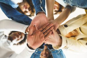 A group of people join hands over the camera with smiles on their face. This could represent the support an anxiety therapist in Arcadia, AZ can offer from the comfort of home. Learn more about online anxiety treatment in Arcadia, AZ and other services today.