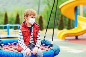 A child wears a mask while sitting alone on playground equipment. Learn how an anxiety therapist in Arcaida, AZ can help you overcoming isolation. Contact a therapist in Arcadia, AZ today to learn more about online anxiety treatment in Arcadia, AZ and more!